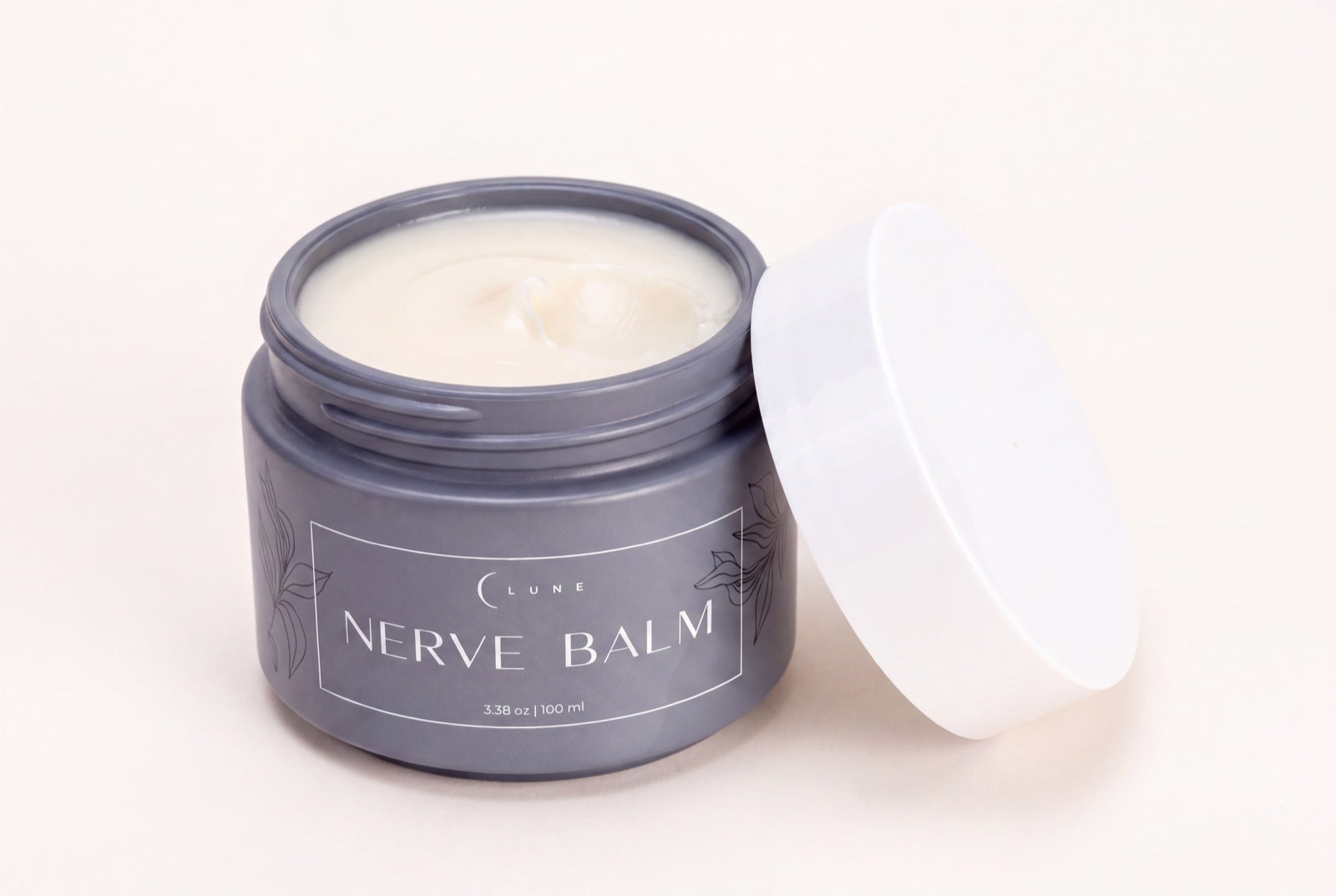 An open jar of Lune Nerve Balm on a wooden nightstand in warm lamplight, the white lid resting beside it.