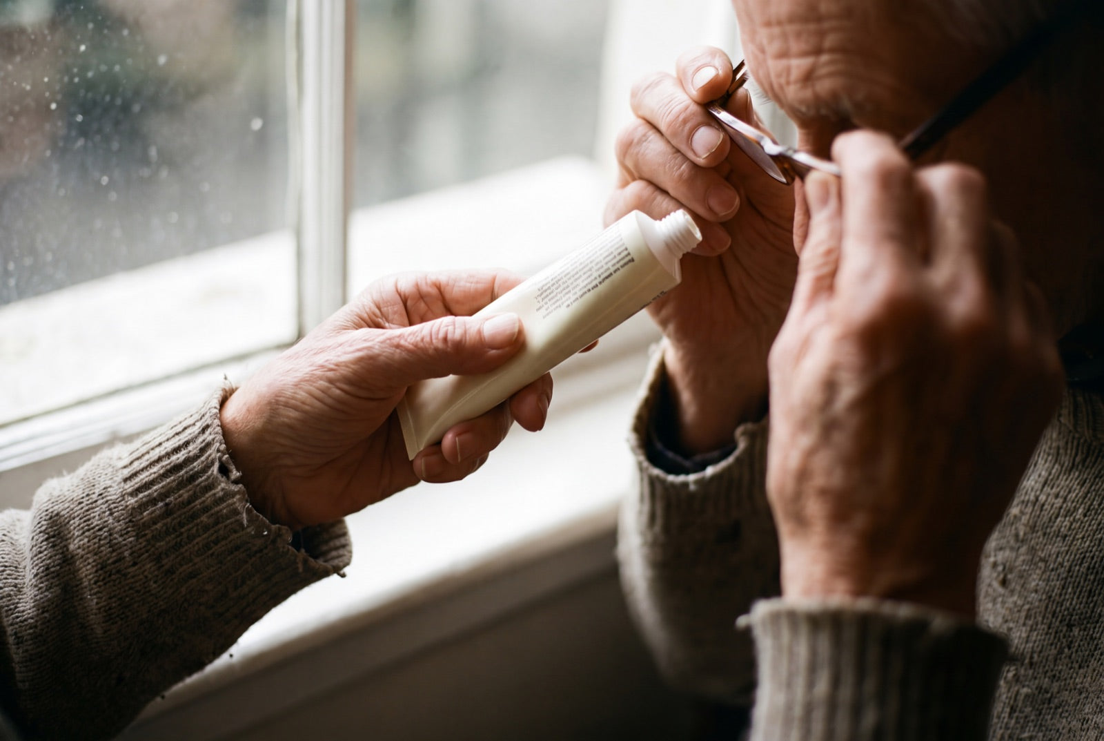 An older person's hands holding a cream tube up close to read the small print on the back.